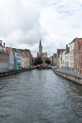 Fototapeta na wymiar Canal lined with houses in Bruges, Belgium with Pootersloge in the distance. Water canal with old houses in Belgium, Europe.