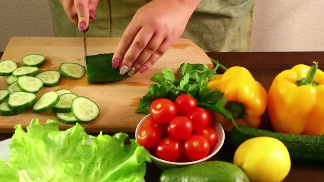 A woman is running a cucumber to prepare a vegetable salad. Shot with dolly from right to left.