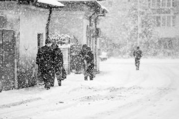 Snowing urban landscape with people passing by
