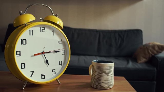 Young man puts the cup of tea on shelf. Big yellow clock is ticking