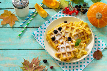 Breakfast table with pumpkin waffles, milk and fresh blackberry berries on a wooden kitchen table.