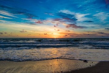 Obraz premium blue sky above the sun rising on the horizon and reflecting off the water on a windy morning at the beach