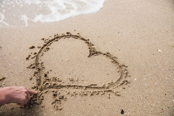 Hand Drawing Heart Shape on Sand