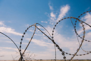 wire and blue sky with clouds. Safety fence of barbed wire against the blue sky