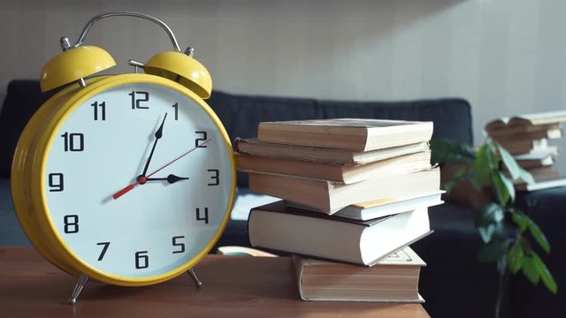 Male hand takes the book off the shelf. Big yellow clock is ticking
