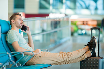 Young man in an airport lounge waiting for flight aircraft. Caucasian man with smartphone indoor