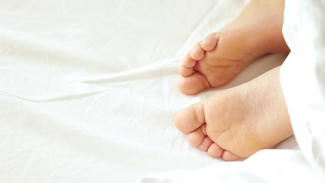 Little kid bare feet nervously quivering in a dream on a white sheet