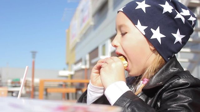 Little girl eating a hamburger. Cute little girl eating a hamburger in the street cafe.