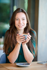 Beautiful elegant girl having breakfast at outdoor cafe. Happy young urban woman drinking coffee