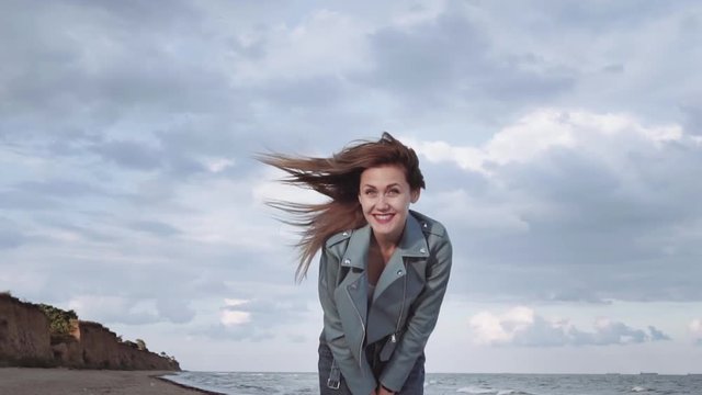 Beautiful, nice girl smiles into the camera and laughs at the seashore on a warm autumn day