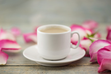Cup of coffee on rustic wooden table in a frame of pink roses. Greeting card with flower. Soft focus.