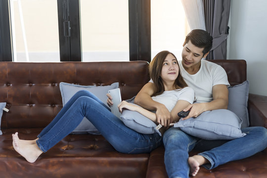 Young couple in love sitting on a brown sofa and watching television.