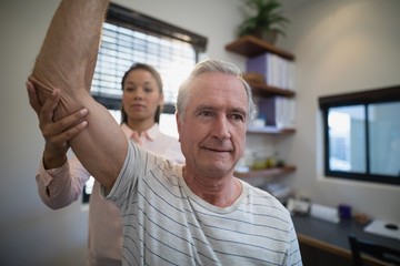 Senior man looking away while female doctor examining elbow