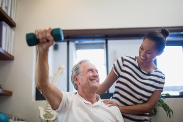 Obraz premium Smiling senior male patient lifting dumbbell while looking at