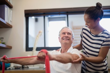 Obraz premium Smiling senior male patient pulling red resistance band while