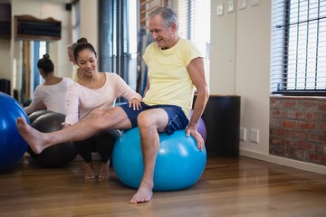 Female therapist helping senior male patient doing leg exercise