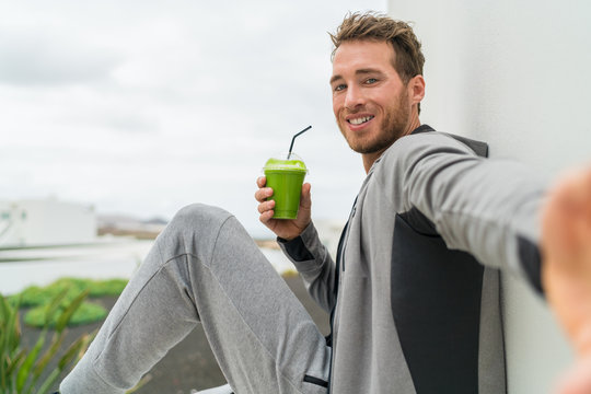 Healthy green smoothie selfie sport fitness man taking self portrait picture at gym drinking vegetable juice after workout in sweatpants and sportswear.