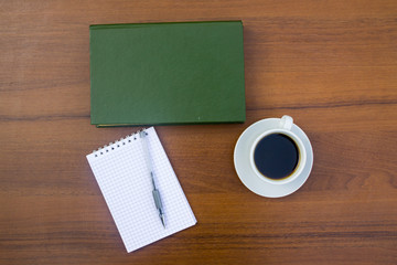 Cup of coffee, book, notepad and pen on wooden desk