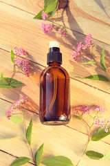 cosmetic  serum with  extract of flowers. Serum in a brown glass bottle on a wooden background with pink flowers and green leaves. Bio vegan vegetable natural cosmetics concept