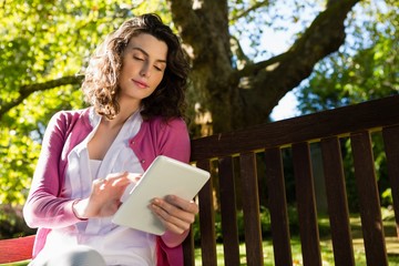 Fototapeta premium Woman sitting on bench and using digital tablet in garden