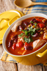Mexican chili chicken stew with beans, corn and tomatoes close-up in a bowl. vertical