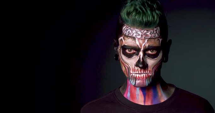 Man with colored skull makeup showing evil smile. Zombie man isolated on black background.