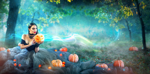 Halloween witch with a carved pumpkin and magic lights in a dark forest