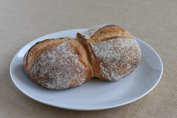 Front View of fresh Rustic Bread Roll on a white plate and tan  background.
