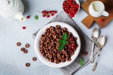 Healthy breakfast with chocolate corn rings, red currant berries, yogurt and tea on a gray concrete background. Selective focus. Top view. Copy space.
