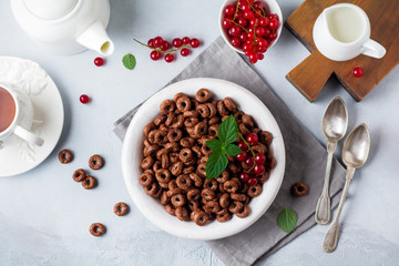 Healthy breakfast with chocolate corn rings, red currant berries, yogurt and tea on a gray concrete background. Selective focus. Top view. Copy space.