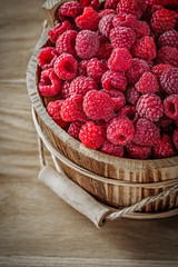 Ripe raspberries in bucket on wooden board