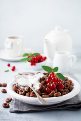 Healthy breakfast with chocolate corn rings, red currant berries, yogurt and tea on a gray concrete background. Selective focus. Copy space.