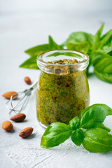 Homemade delicious green pesto in a glass jar. On a gray concrete background. Traditional Italian sauce. Selective focus.
