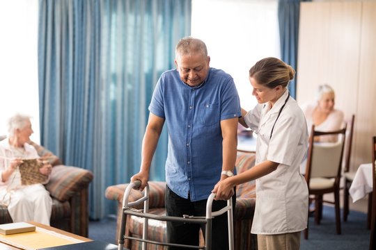 Female doctor assisting senior man walking with walker