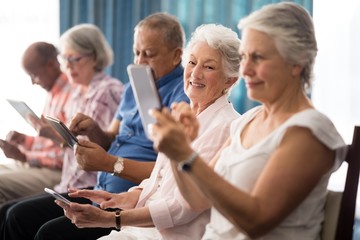 Fototapeta premium Senior people sitting on chairs while using digital tablets