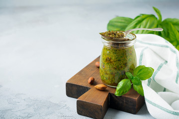 Homemade delicious green pesto in a glass jar. On a gray concrete background. Traditional Italian sauce. Selective focus.