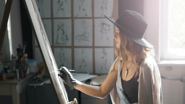 Lovely female artist, in a black smart hat, drawing a picture at the easel, slow motion