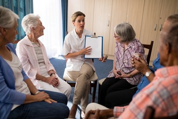 Female doctor explaining with clipboard to seniors sitting on