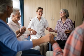 Obraz premium Smiling female doctor holding hands with seniors while sitting