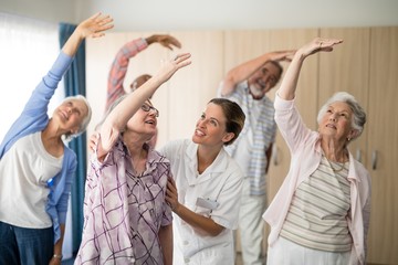 Smiling female doctor assisting senior woman exercising