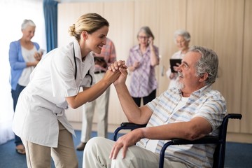 Smiling female doctor holding hands with disabled senior man