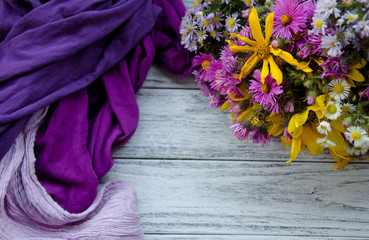 Bouquet of bright autumn flowers and pile of scarves forming a frame on a gray wooden background (with copy space in the center for your text), selective focus