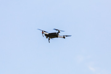 A beautiful modern black drone quadrocopter with the photo and a video camera on the board flies against the blue sky