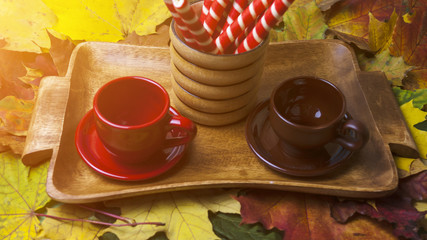 two cups and sweets on a wooden tray against the background of autumn leaves