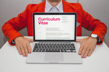 Man showing curriculum vitae on laptop. Foreign text is latin. Text meaning: generic CV pre filled. All data showing a generic format for cv, without reference to someone or somewhere.