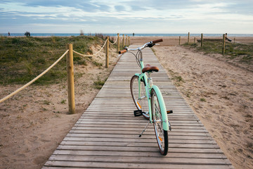 Fototapeta na wymiar Lonely beautiful mint bike on wooden boardwalk to sea with soft sunset