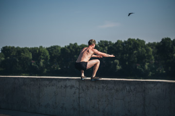 Shirtless athlete working out on cross fit jump box outside on a wall. Muscular man doing box jumps outdoors.
