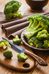green broccoli on a cutting board with a knife over wooden background