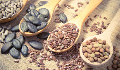 Flaxseed, pumpkin, raisins, lentils and sunflower seeds in wooden spoons.