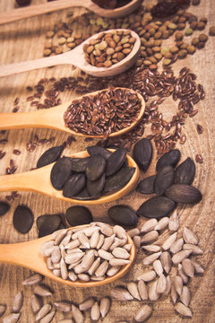 Flaxseed, pumpkin, raisins, lentils and sunflower seeds in wooden spoons.